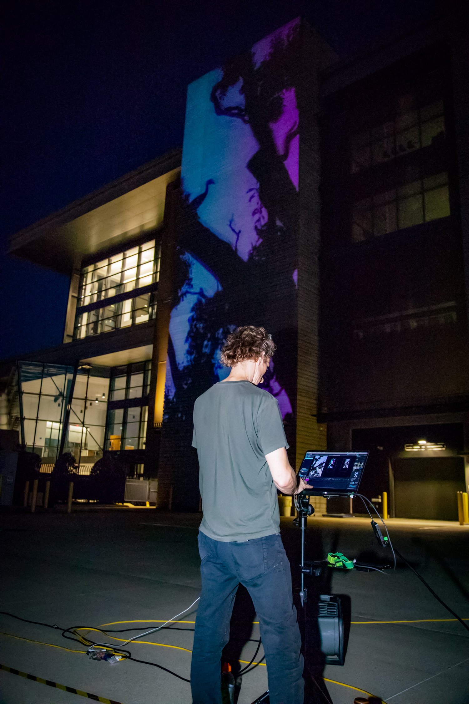 Chad Mount works at a projection control station in front of the illuminated OSU Discovery façade.