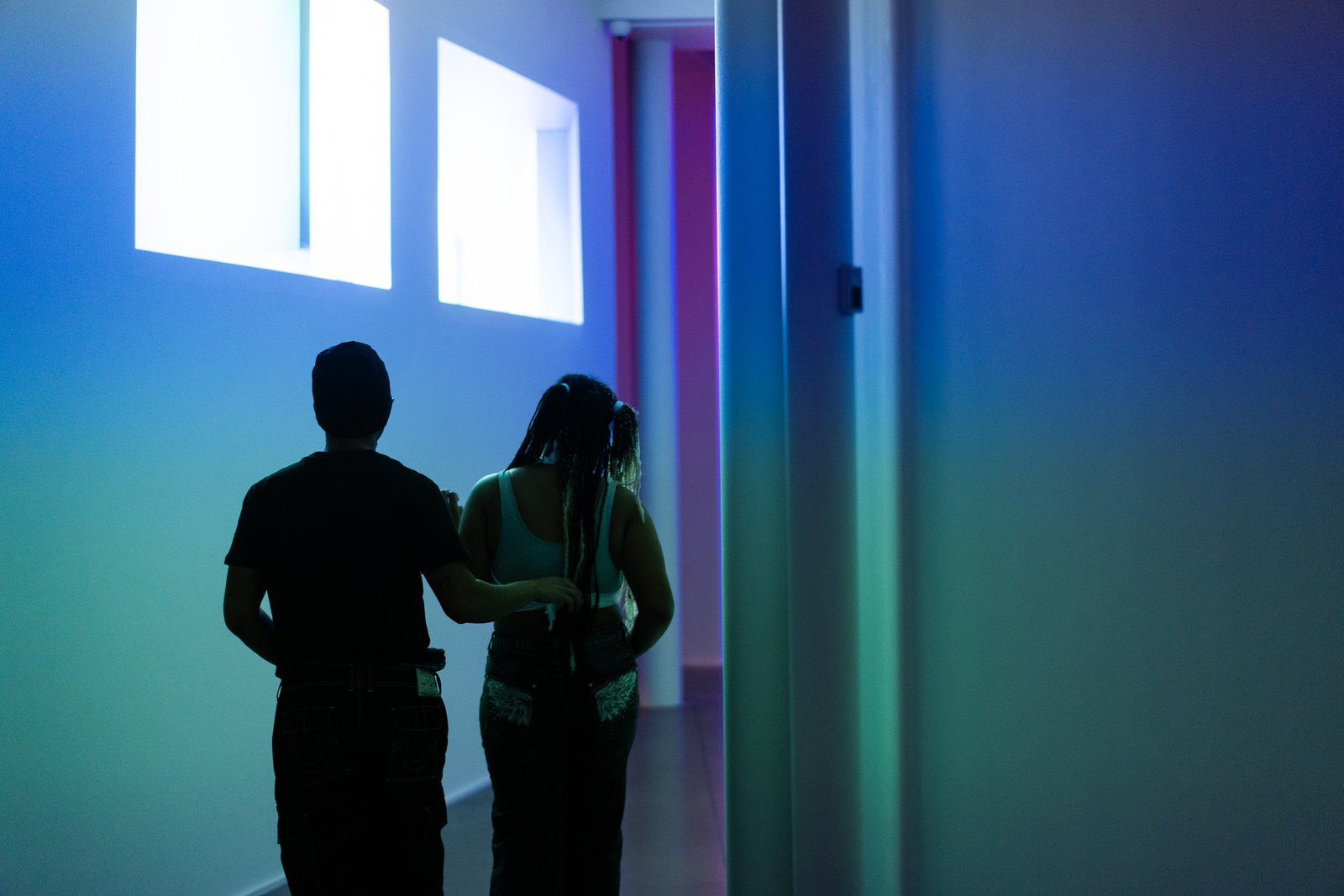 Two visitors move through a blue-lit gallery while viewing Lumaform.