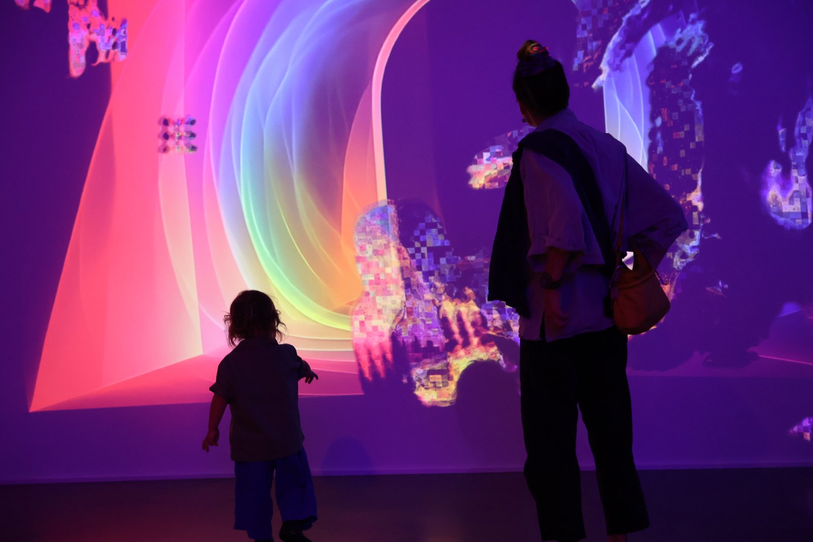 An adult and child stand before the responsive projected light and color of Portal Field.