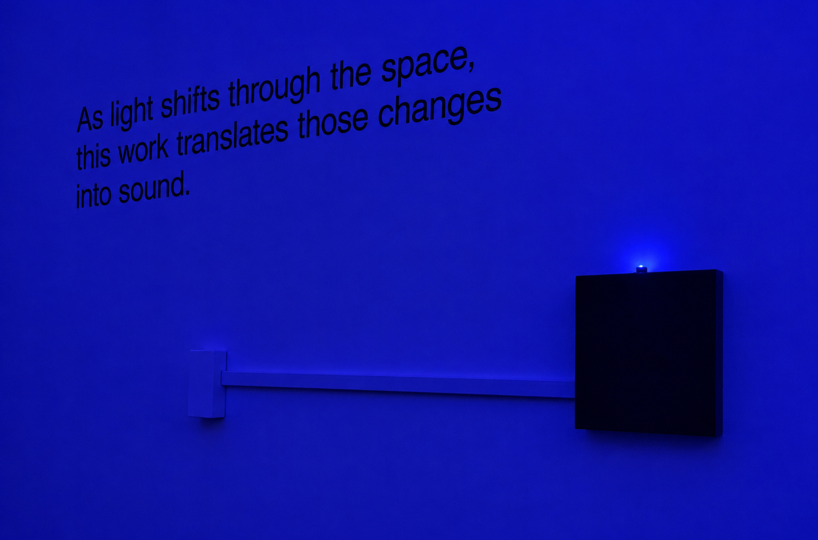 Prana-Luma projects text across a blue-lit gallery wall beside a sound cabinet.