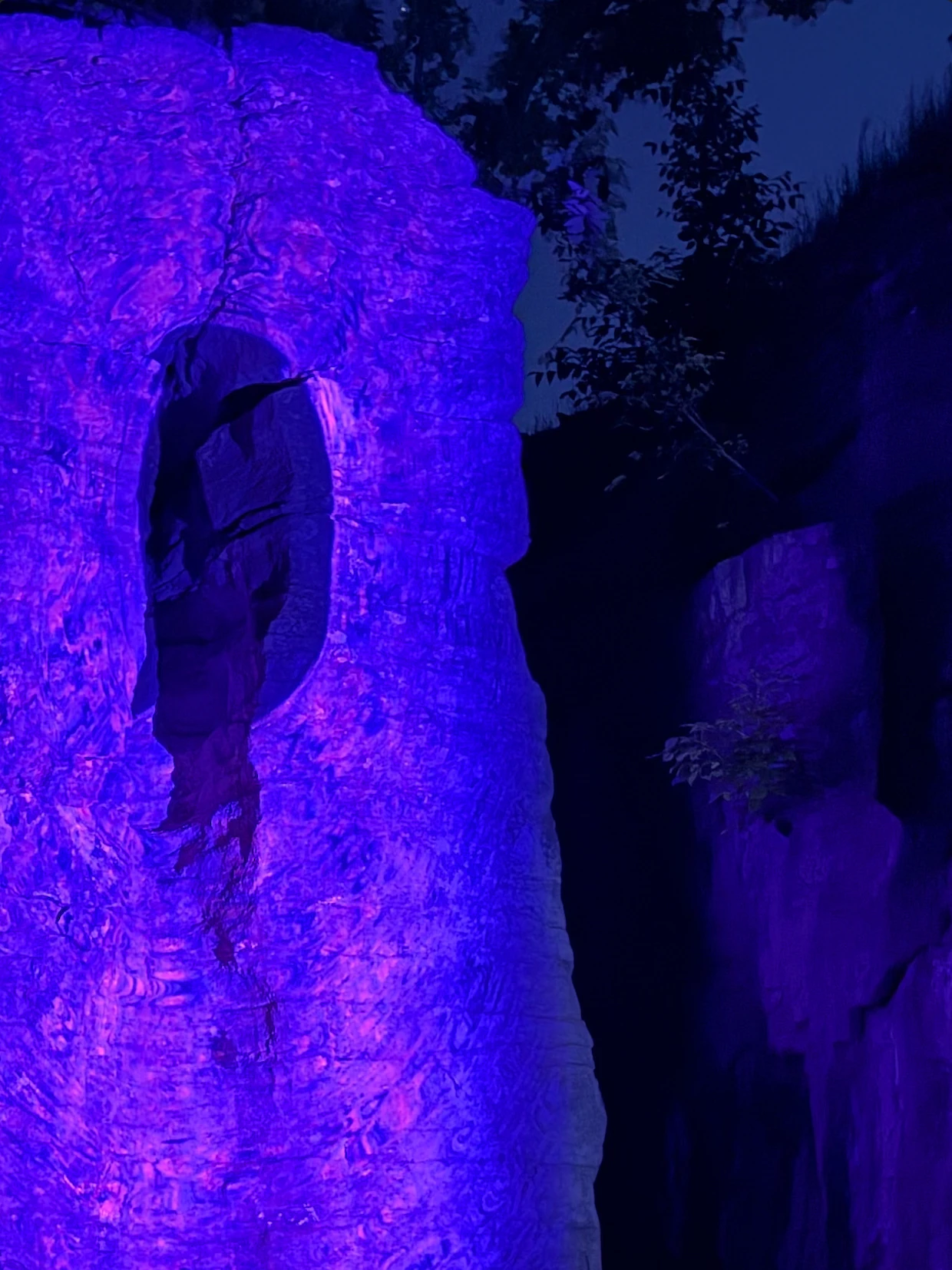 Violet projected light surrounds a dark opening in a rock face at night, forming a second portal. Photograph by Rob Helms.