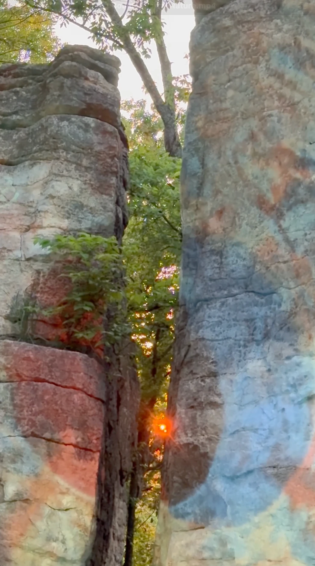 Projected color crosses two boulders as the setting sun glows through the opening between them.