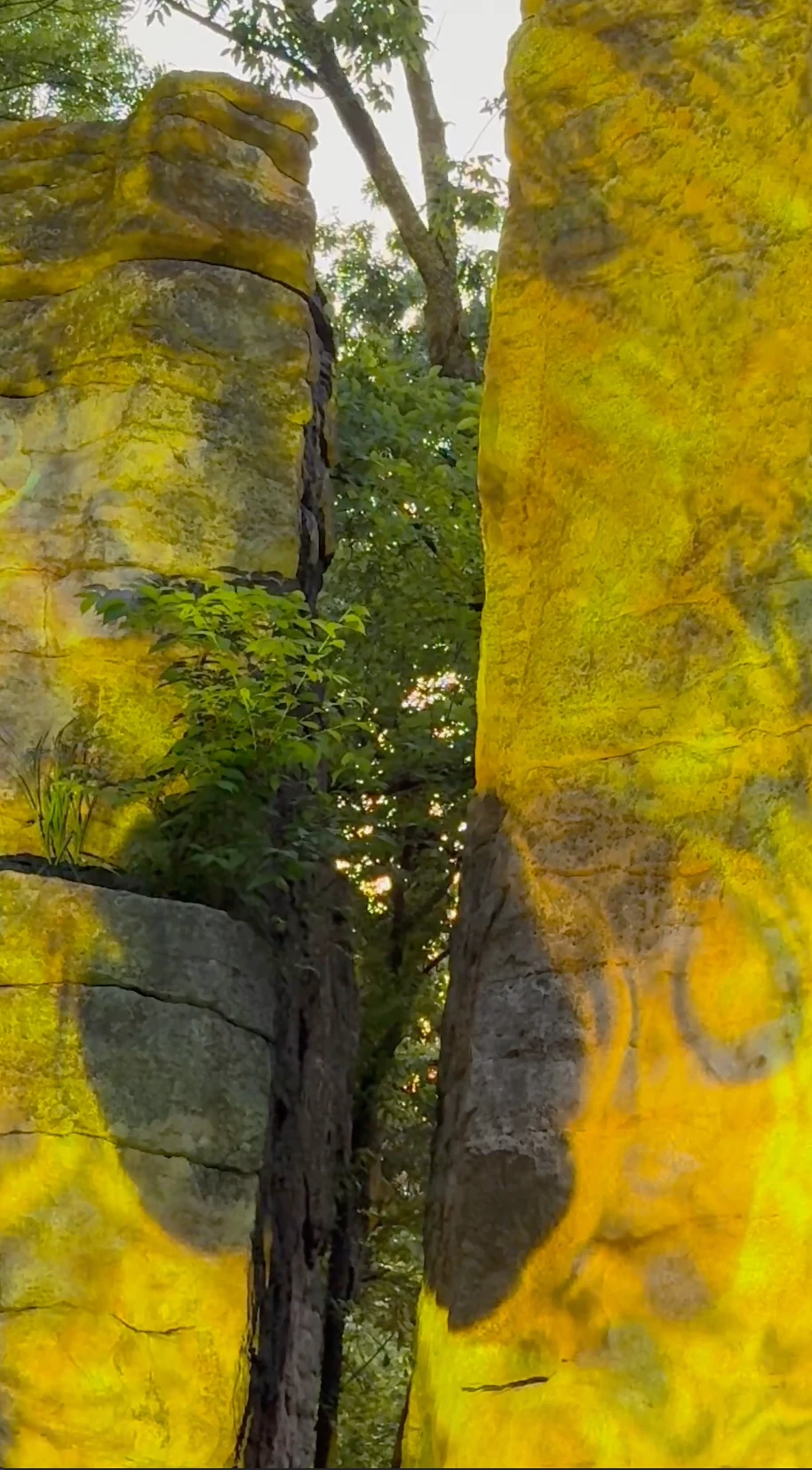 Golden projected patterns illuminate the two boulders and their narrow opening.