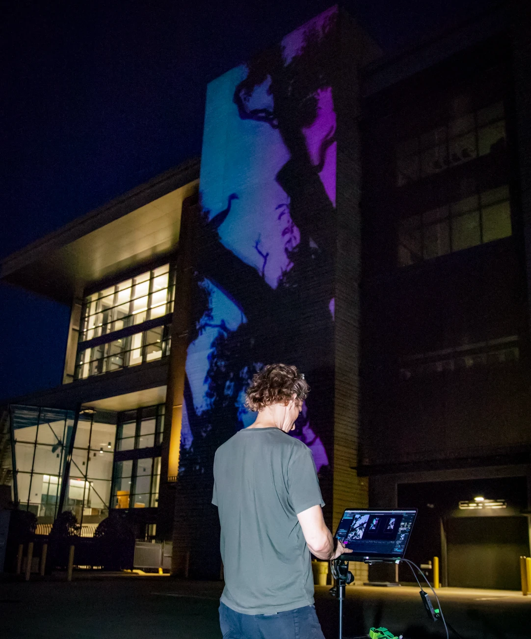 Chad Mount works at a projection control station in front of the illuminated OSU Discovery façade.